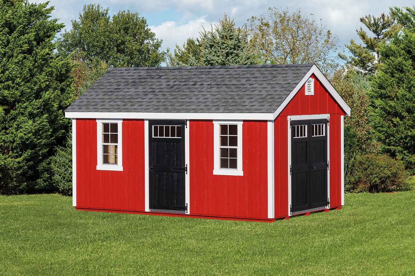 Red storage shed with black doors and windows on a grassy area with trees in the background