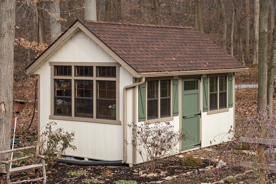 Small white building with a brown roof in a wooded area