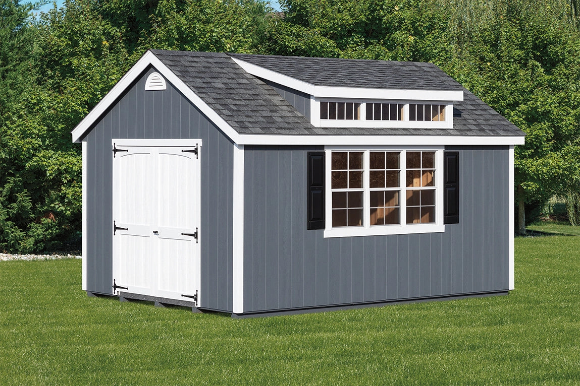 Gray storage shed with white doors and windows on a grassy area with trees in the background