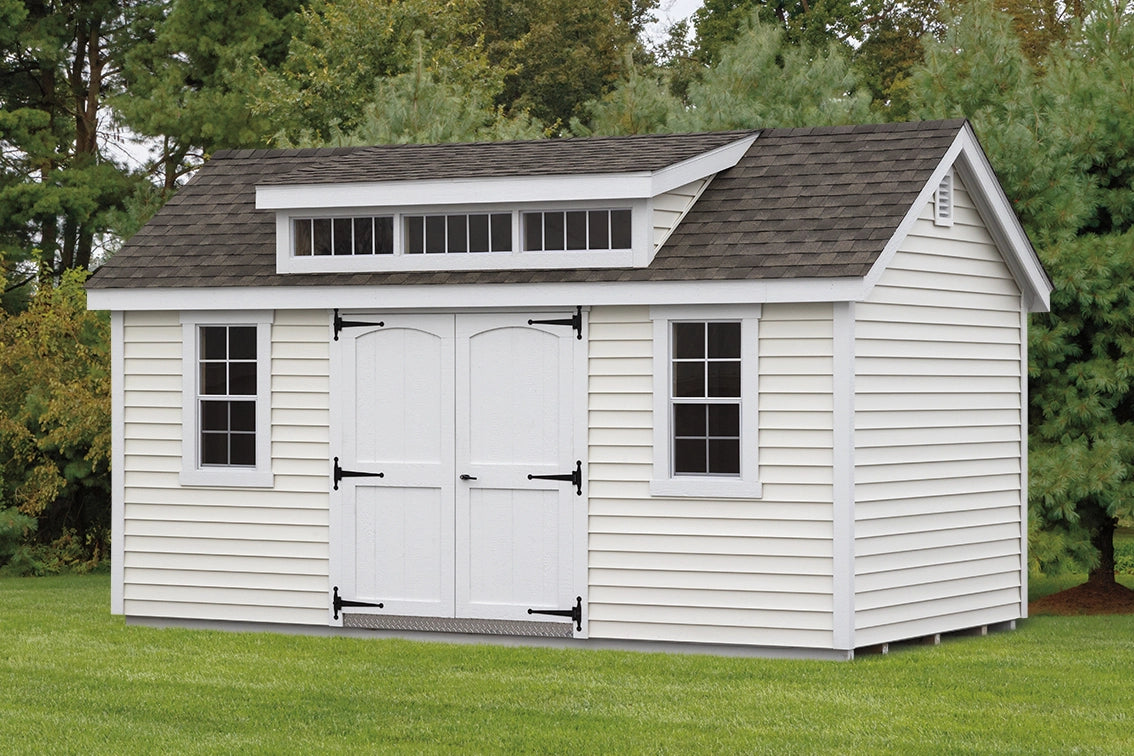 White storage shed with gray roof on a grassy area with trees in the background