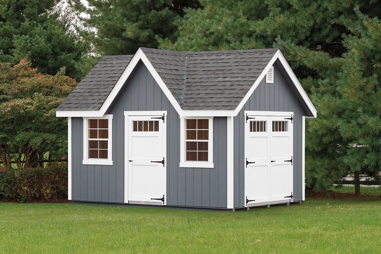 Small gray shed with white doors and windows on a grassy area with trees in the background