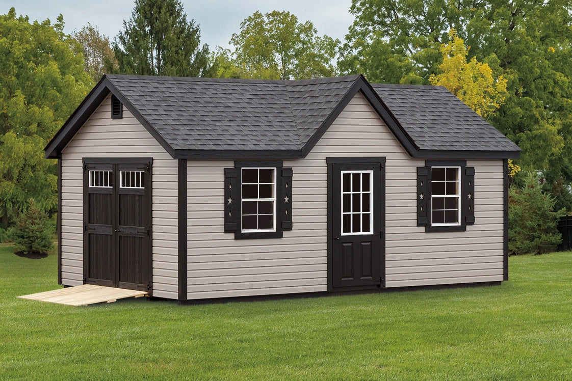 Small storage shed with black roof and white walls on a grassy area with trees in the background