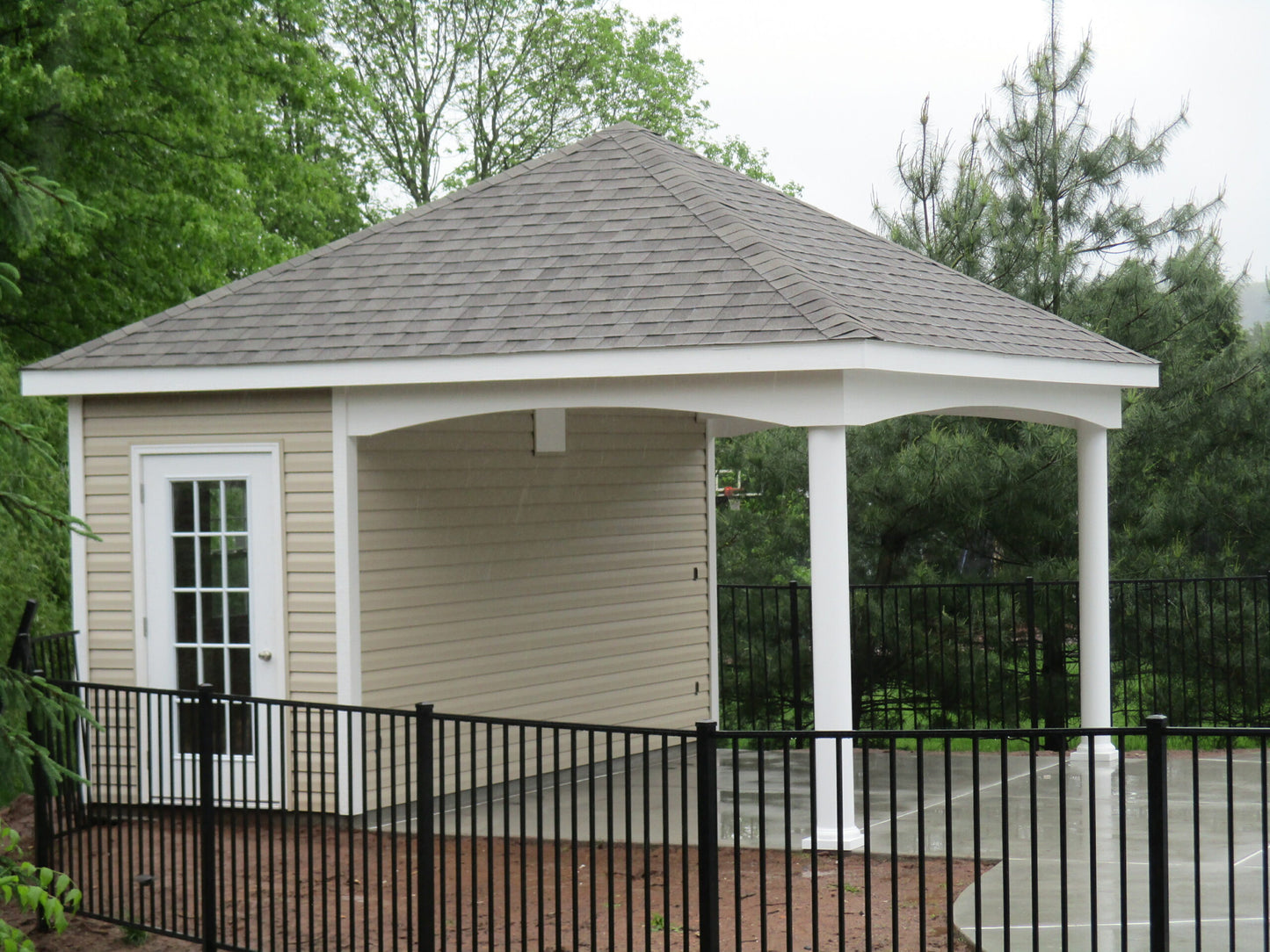 Gazebo with a shingled roof and white columns in a park-like setting.