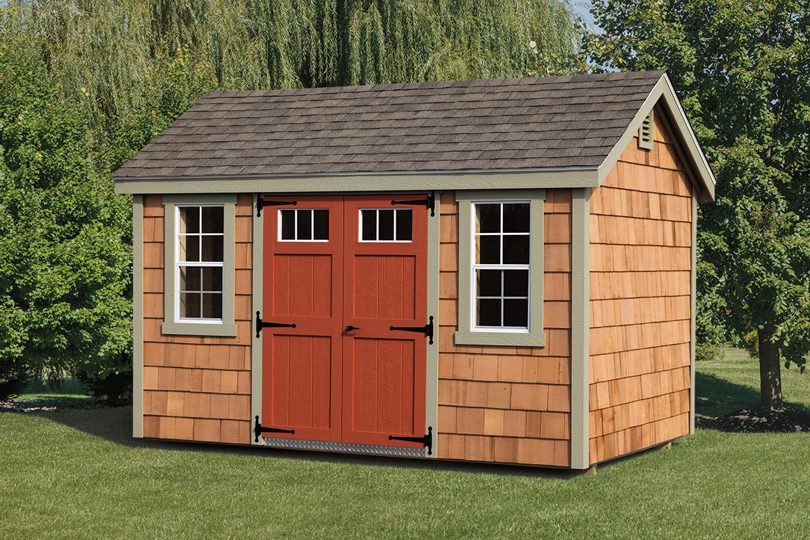 Wooden shed with red doors and brown shingles on a grassy area with trees in the background