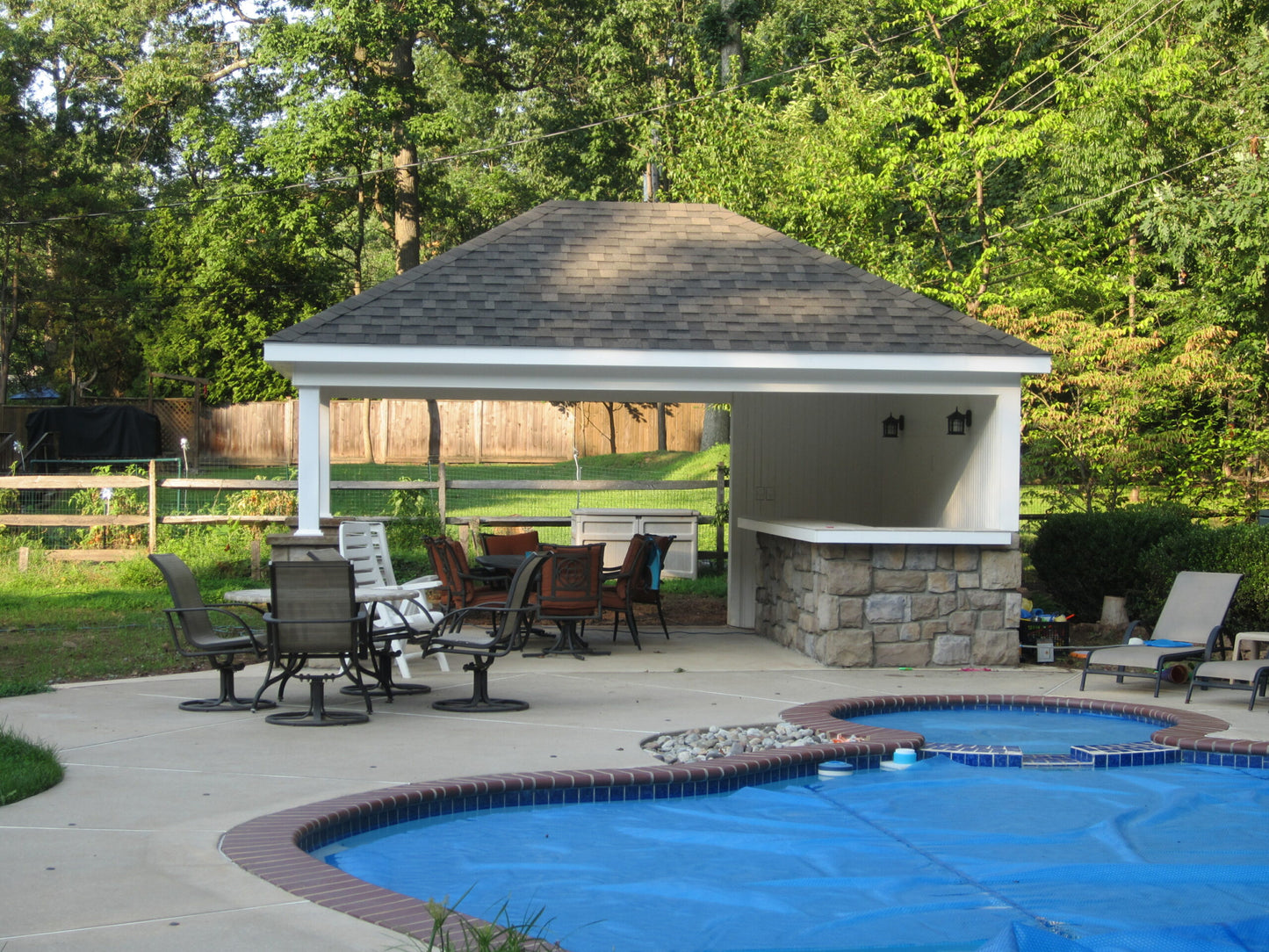 Outdoor gazebo with dining area next to a pool in a backyard setting.