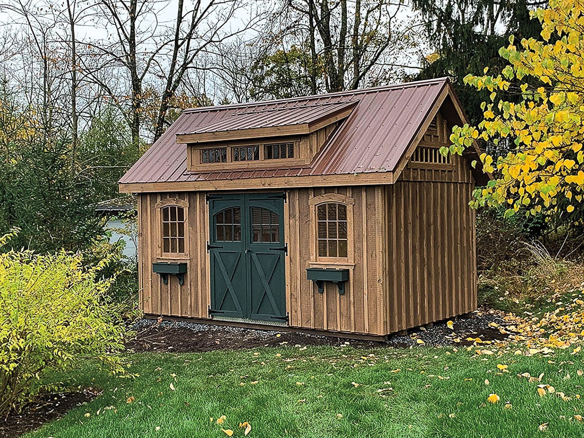 Wooden shed with a brown roof in a garden setting with trees and grass.