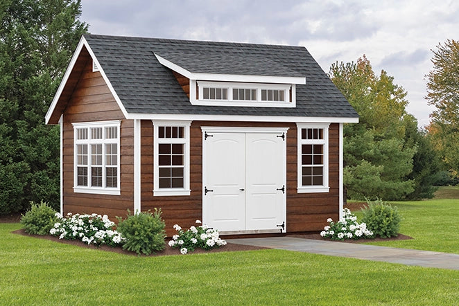 Small wooden house with white doors and windows, surrounded by greenery.