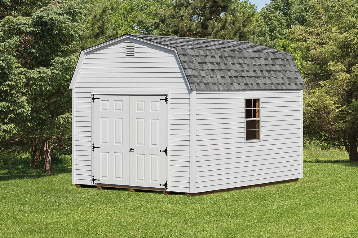 White storage shed with a gray roof on a grassy area with trees in the background