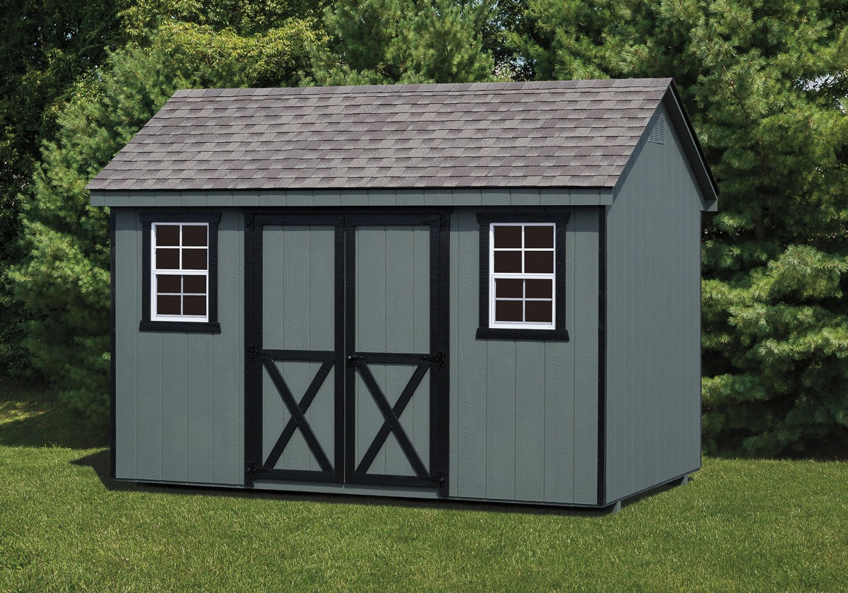 Gray storage shed with a shingled roof in a grassy area with trees.