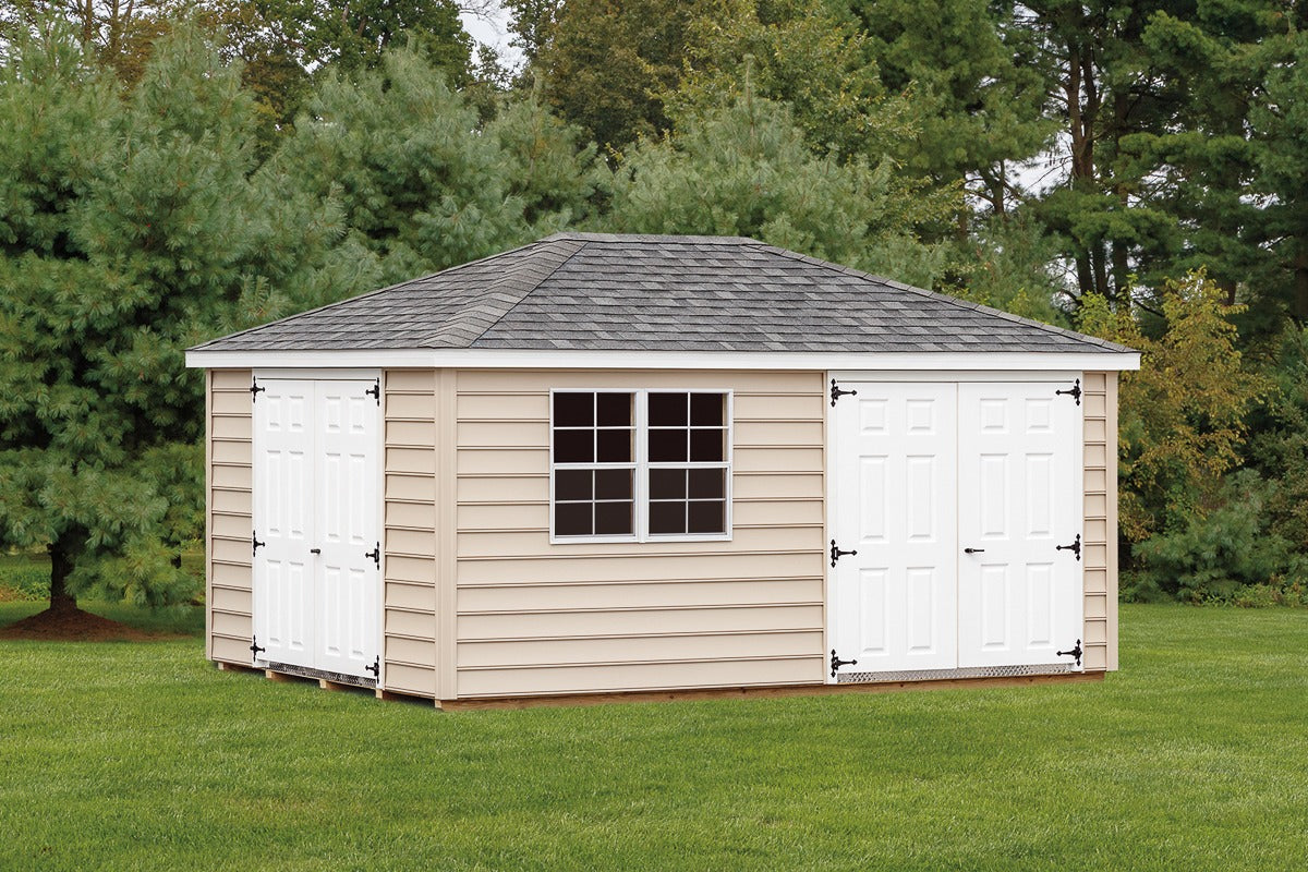 Wooden shed with white doors and a window on a grassy area with trees in the background