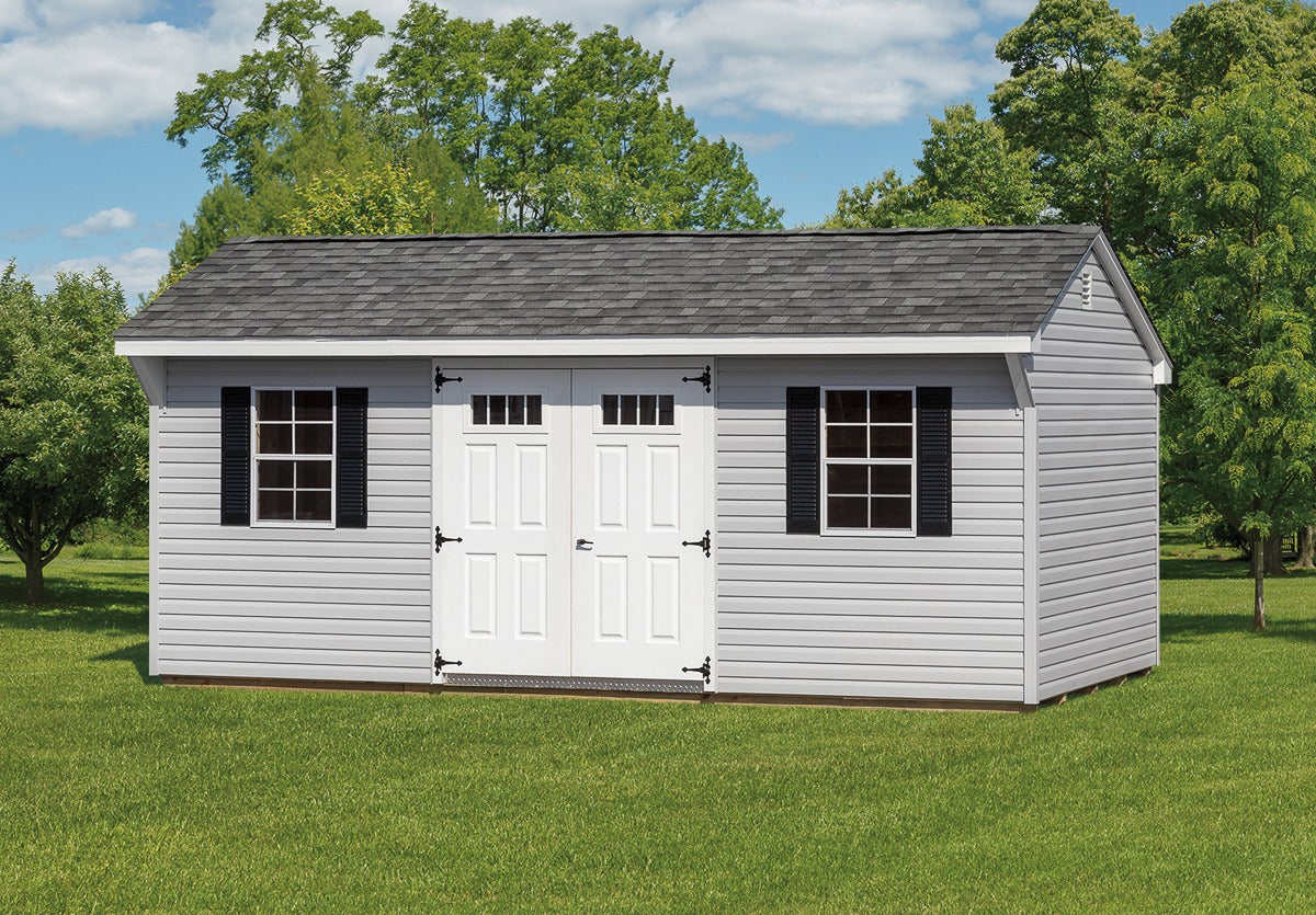 White storage shed with black shutters on a grassy area with trees in the background