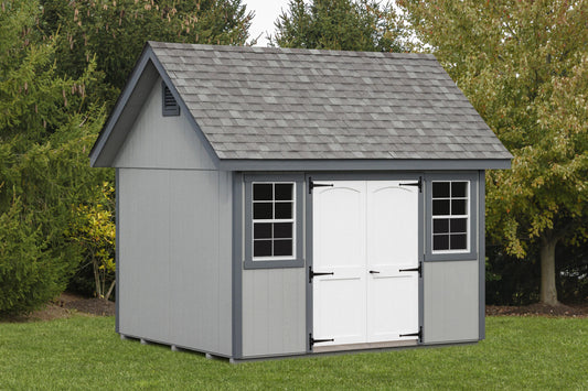 Gray storage shed with white doors on a grassy area with trees in the background