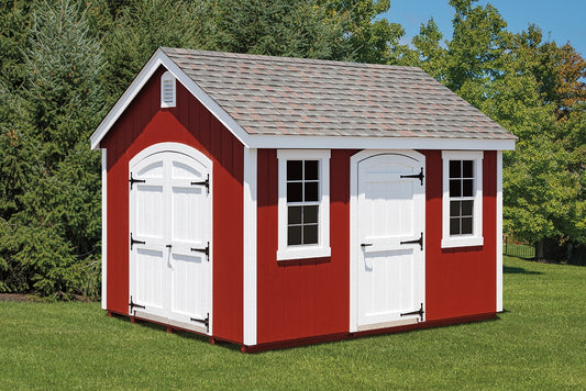 Red and white storage shed with a gray roof in a grassy area with trees.
