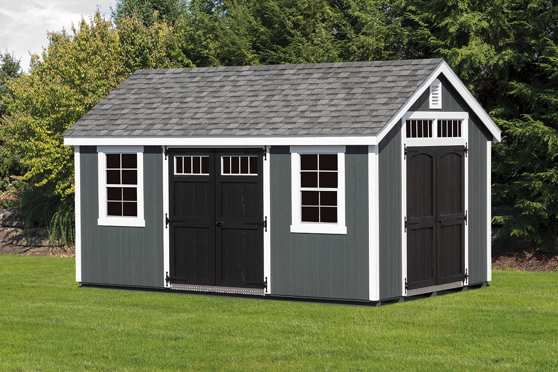 Gray storage shed with black doors on a grassy area with trees in the background