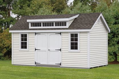 White storage shed with gray roof on a grassy area with trees in the background