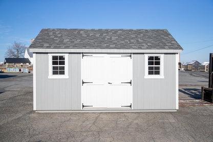 Small storage shed with a white door and gray roof on a clear day.