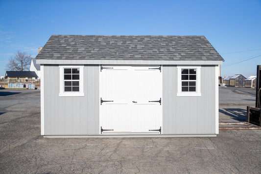 Small storage shed with a white door and gray roof on a clear day.