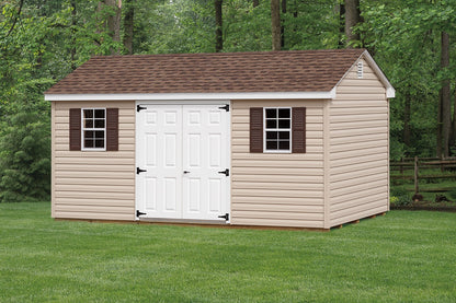Wooden storage shed with a brown roof and white doors on a grassy area with trees in the background.