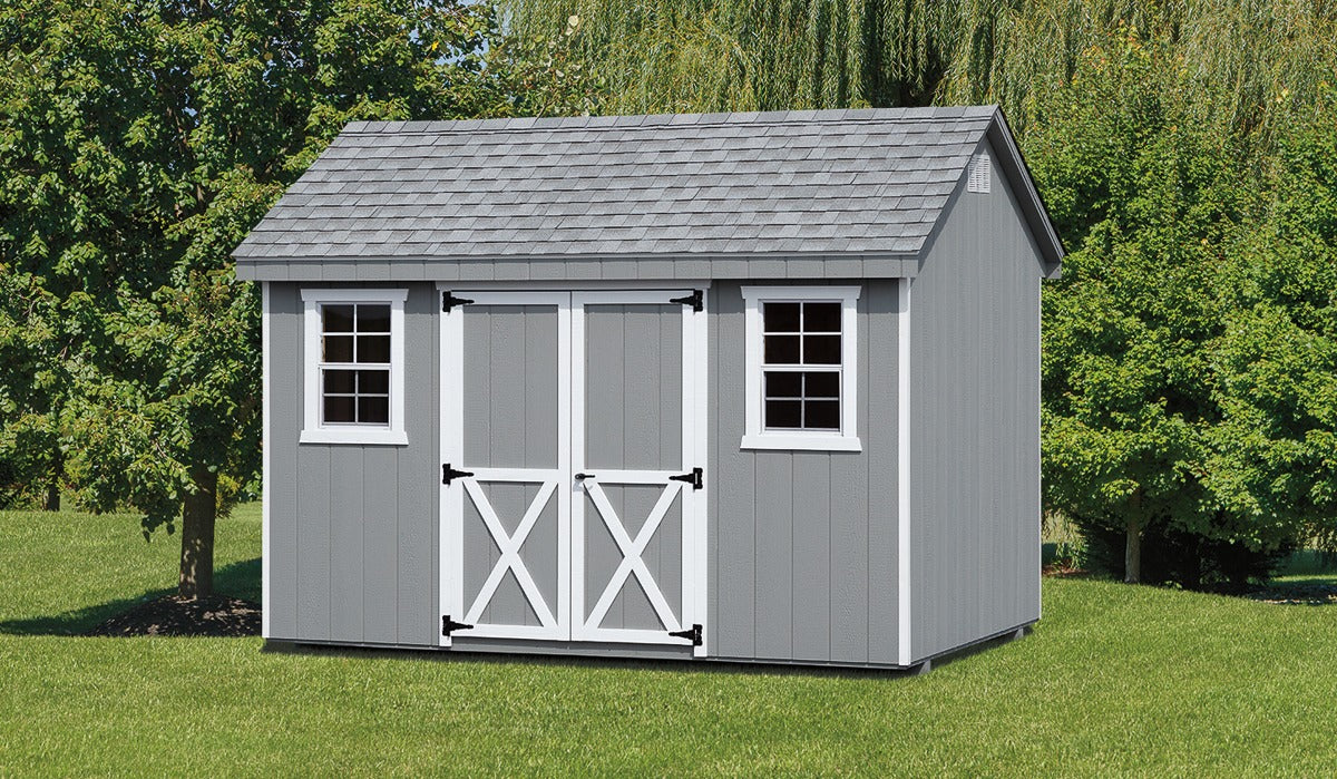 Gray storage shed with white doors and windows on a grassy area with trees in the background
