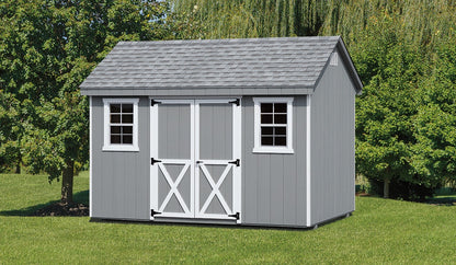 Gray storage shed with white doors and windows on a grassy area with trees in the background