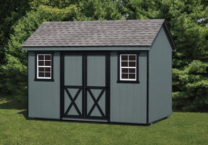Gray storage shed with a shingled roof in a grassy area with trees.