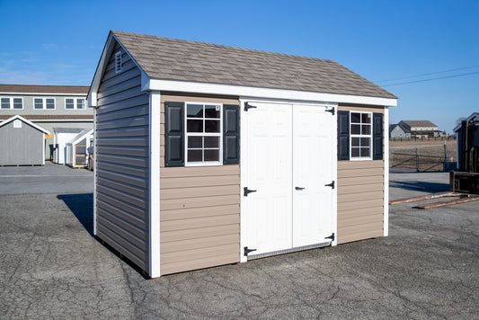 Small storage shed with beige siding and white doors on a clear day.